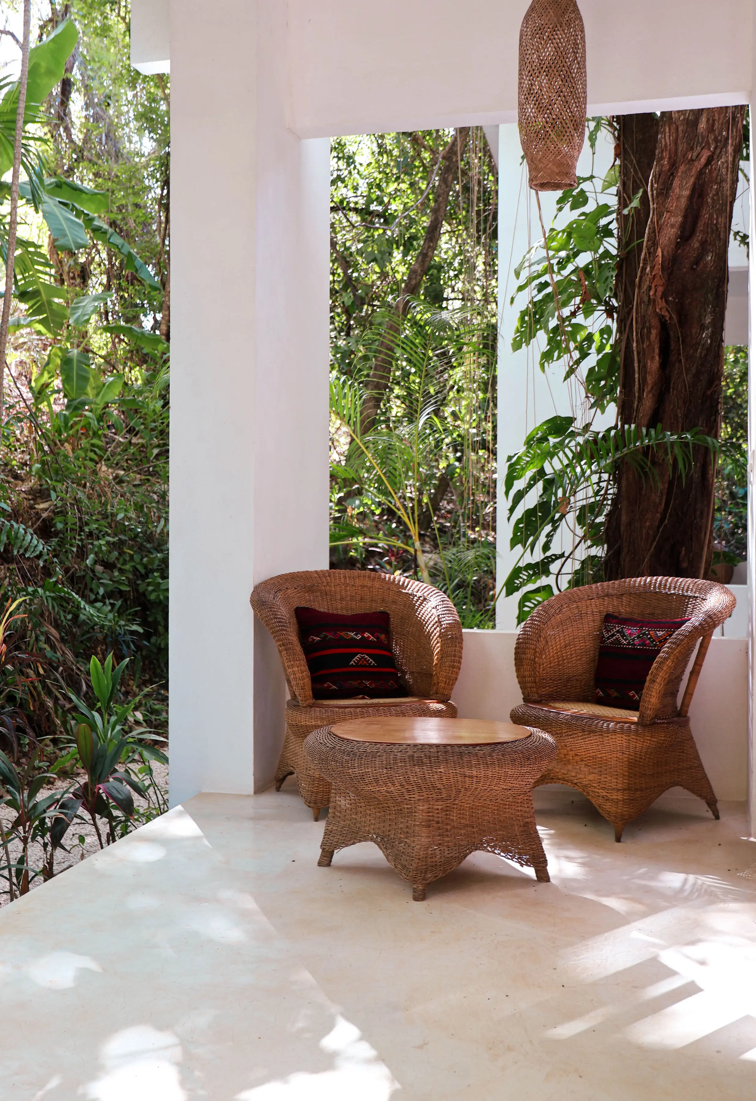 Two wicker chairs and a low table on a casita veranda, open to the jungle